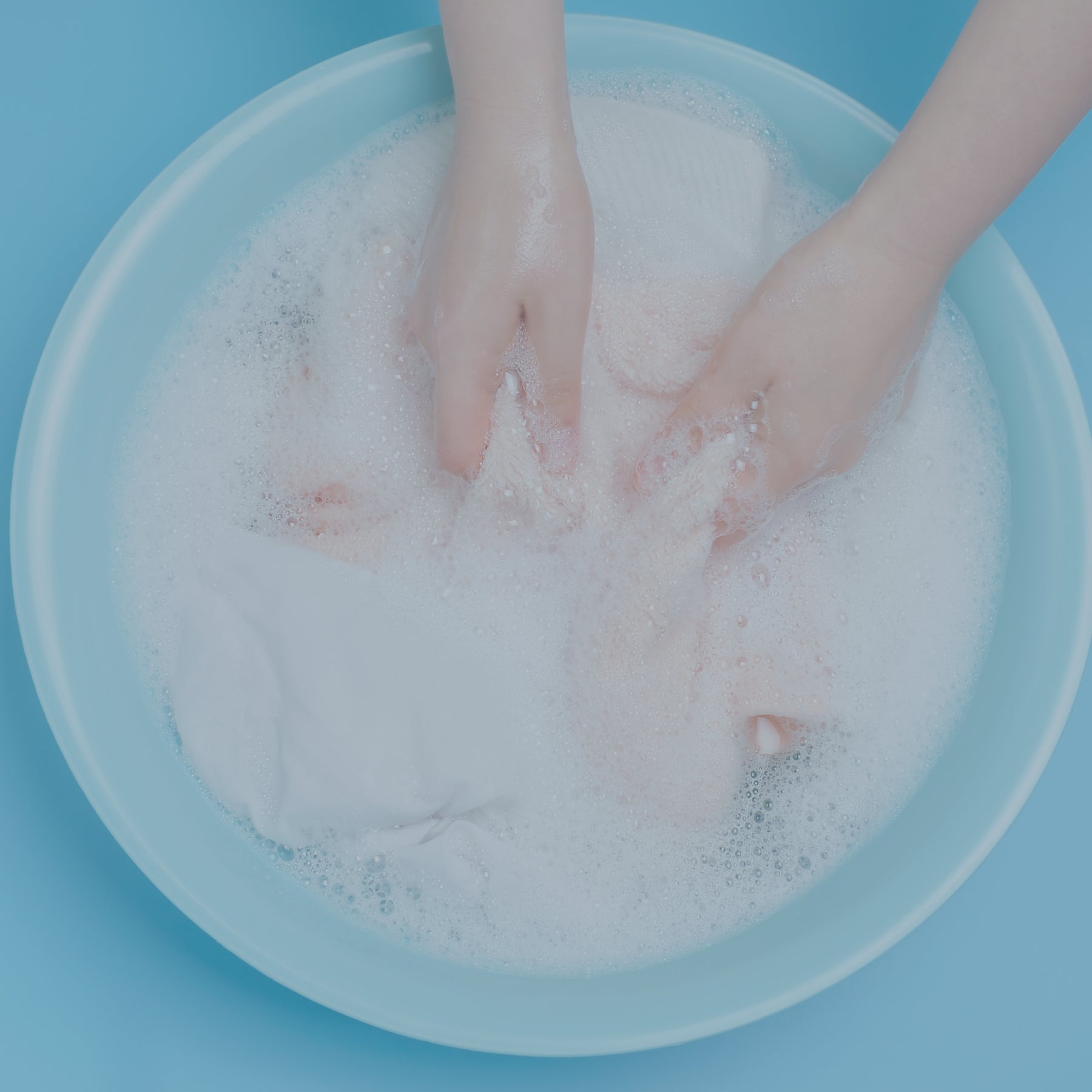 Person hand washing clothing in a soapy bucket